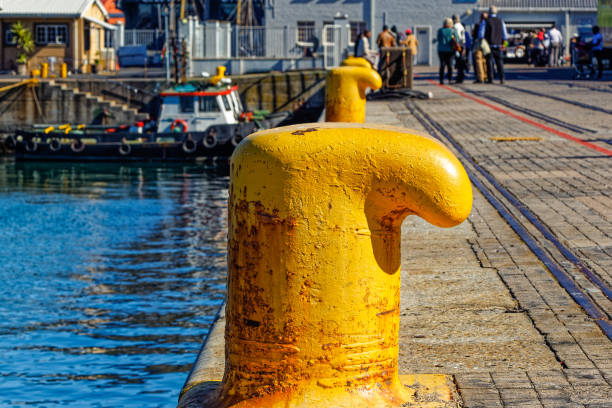 Row of brightly painted yellow cast iron bollards on Cape Town Waterfront with visiting tourists in the background