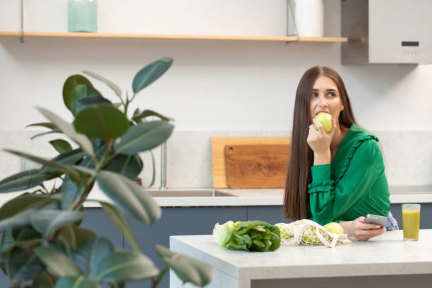 istock An attractive brunette holds a green apple while standing at the kitchen table. 1459368495