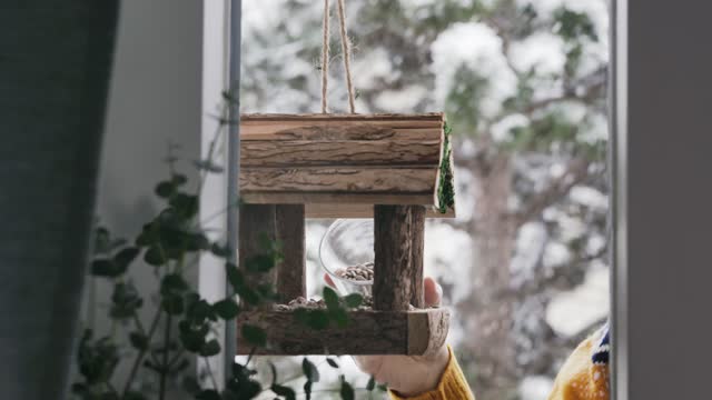 Woman hanging a bird feeder on balcony in winter