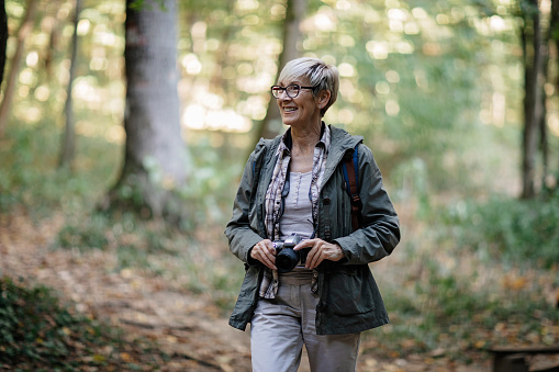 Senior woman hiking while holding vintage camera to photograph