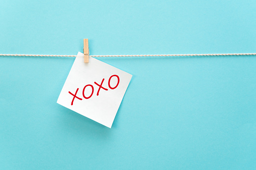 White reminder paper on a rope with a clothespin with a motivational inscription XoXo in handwritten font on a colored background with free space for text