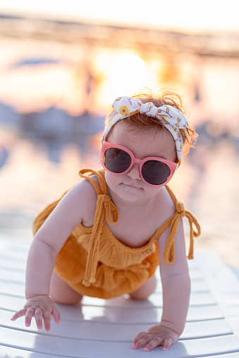 Portrait of fashionable baby crawling on sunbed with sunset in the background.