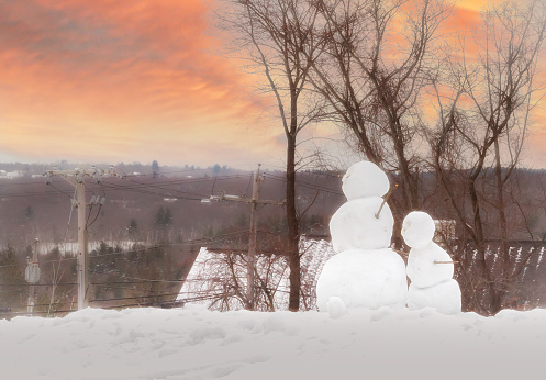 Two snowmen on the hill at sunset