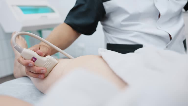 doctor does an ultrasound of the veins on the patient's legs. A phlebologist checks the veins on a woman's legs with an ultrasound machine in a modern clinic.