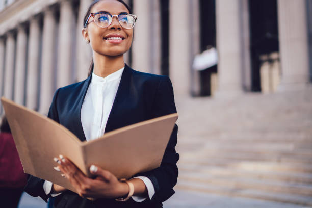 istock Smiling black woman holding open folder with documents and looking away 1459381973