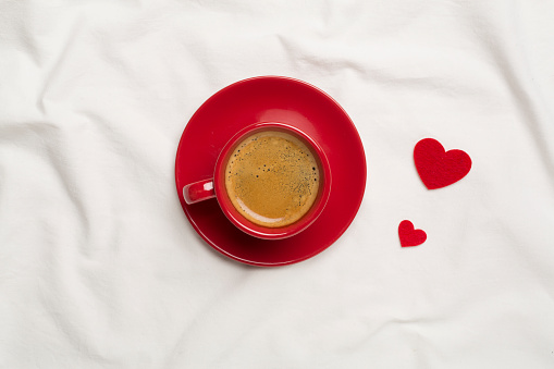 Red cup of coffee with hearts on white sheet, top view