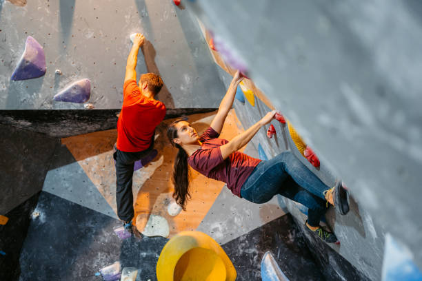 homem e mulher jovens escalando em uma parede de escalada - climbing wall rock climbing holding reaching - fotografias e filmes do acervo