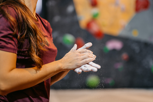 Close-up of a young athletic woman standing in front of an indoor climbing wall and putting chalk on her hands.