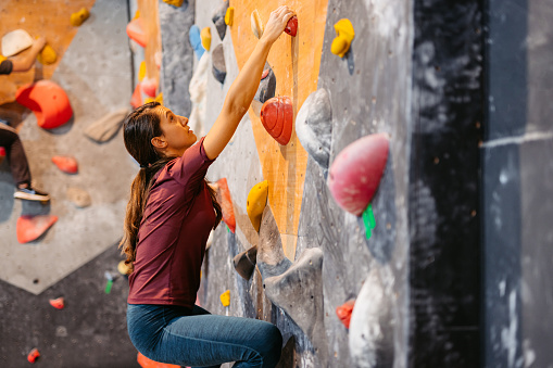 Beautiful young athletic woman climbing on an indoor climbing wall.