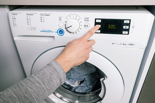 FINGER PRESSING A BUTTON ON THE WHITE WASHING MACHINE TO CHOOSE A WASH FEATURE