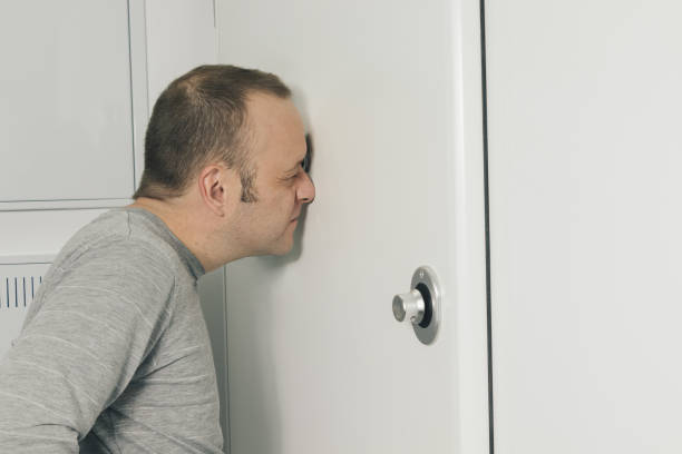 MAN LOOKING THROUGH THE PEEPHOLE OF HIS HOME