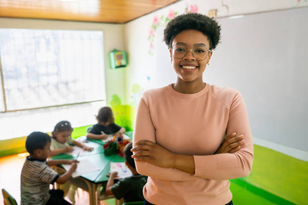 Happy preschool teacher smiling at the school Happy African American preschool teacher smiling in a classroom at the school pre school teacher stock pictures, royalty-free photos & images