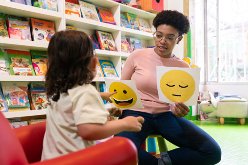 African American teacher teaching a girl about emotions at school and showing her happy and sad faces