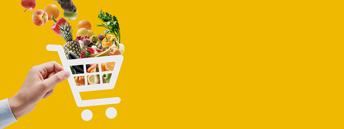 Hand holding a trolley icon full of fresh groceries: online grocery shopping and delivery app