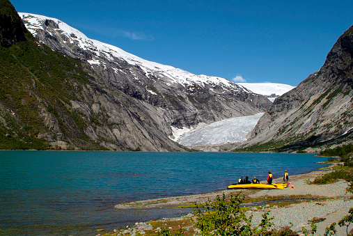 Jostedalen, Norway - June 14, 2009: unknown water sports enthusiasts with kayaks on the lake and the glacier tongue of the Nigardsbreen glacier