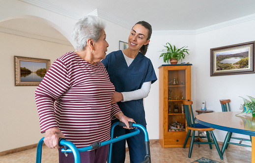 Happy Latin American home caregiver helping a senior woman using a walker at home - assisted living concepts