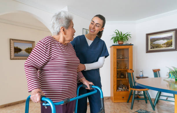 Home caregiver helping a senior woman using a walker at home stock photo