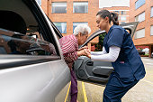 Home caregiver helping a senior woman get out of a car