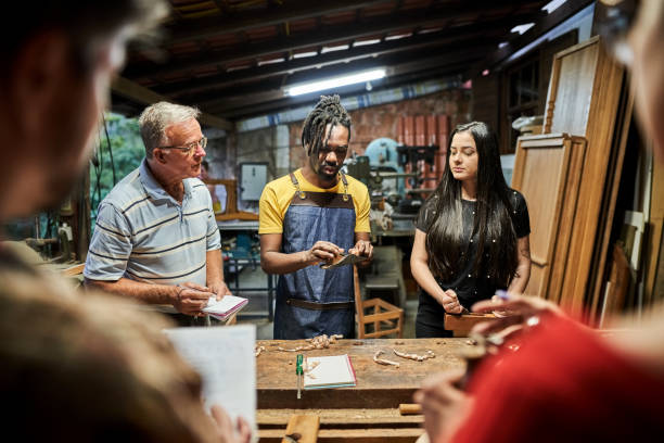 istock Carpenter teaching group of people standing at workbench in woodwork class 1459392598