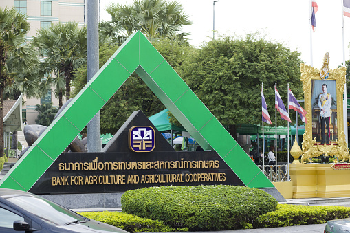 Triangle sign at Bank for Agriculture and Agricultural Cooperatives seated at upper Phahoyothin Road in Bangkok. At right side afre thai flags and an image of King of Thailand