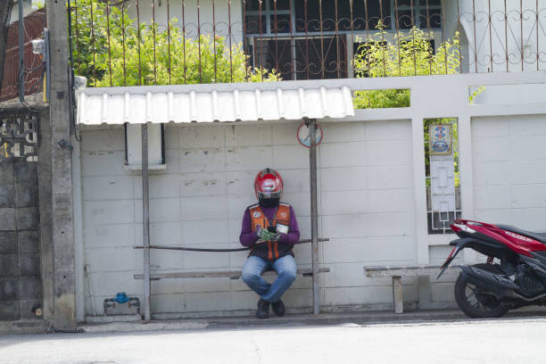 Thai motorcycle taxi driver is sitting at waiting point on a bench in residential district in Bangkok Chatuchak. Scene is in street Soi ladprao Soi 1 a connection shortcut between Ratchadaphisek and Ladprao Roads.