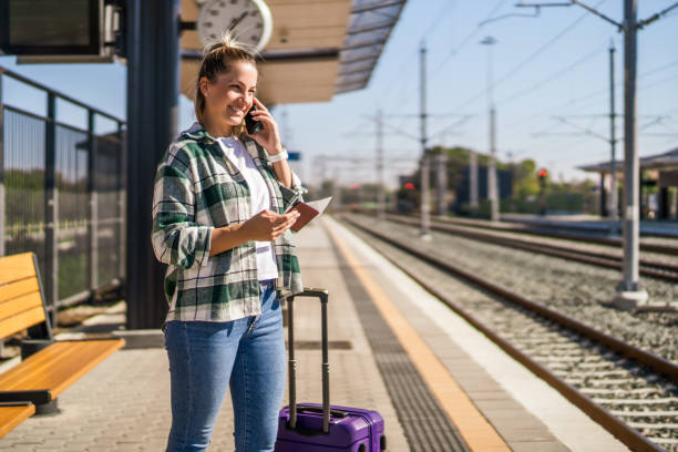 Mulher que usa o telefone móvel e segurando o bilhete em uma estação de trem - foto de acervo