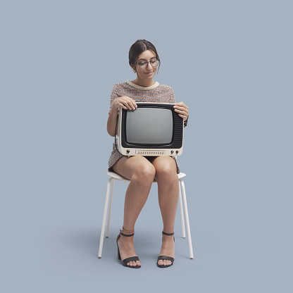 Woman sitting and holding a vintage television, isolated on gray background