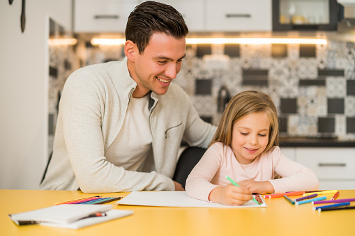 Little girl and her father enjoy drawing together at their home.