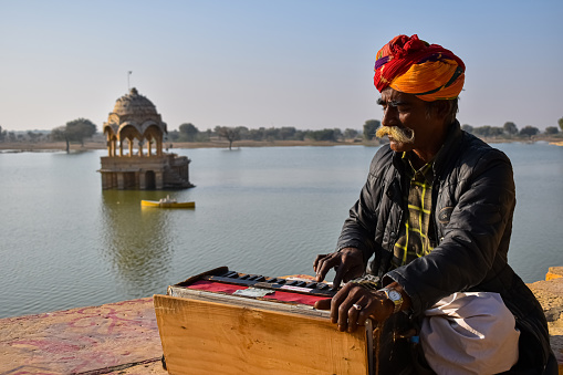 Jaisalmer, Rajasthan India-On 4th February 2020 local man was singing a beautiful traditional Rajasthani folk song with a harmonium on the edge of Gadisar lake during sunset.