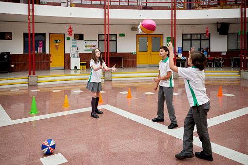 Full length view of elementary age children aged 10 and 11 wearing uniforms and exercising indoors during recreation break.