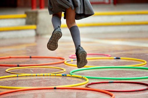 Low angle view of elementary age schoolgirl in mid-air while jumping from hoop to hoop during recreation break.