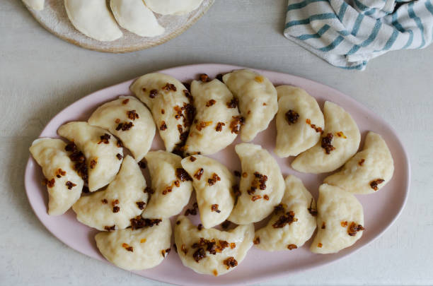 Boiled Vareniks stuffed with potatoes and fried onions on a pink plate. The concept is traditional Ukrainian cuisine. Horizontal orientation. Top view. stock photo