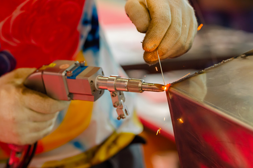 Welder hands using portable handheld laser welding machine with sparks - close up. Manufacturing, industrial, equipment, technology and metalworking concept