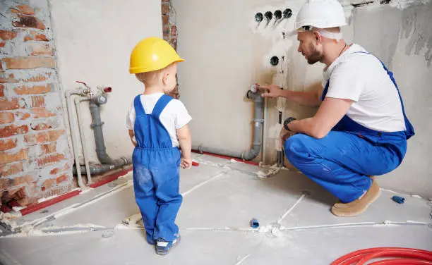 Man and kid working together on home renovation. Father and child in safety construction helmet using manometer or pressure gauge while checking gas tightness of heating system.