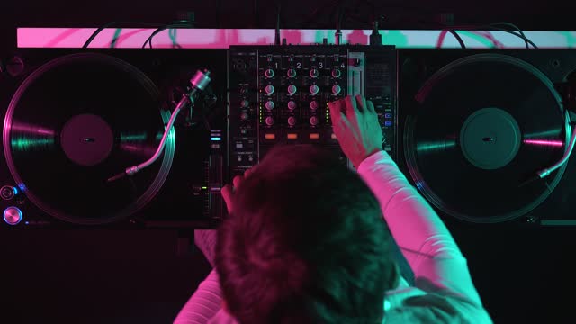 Night club DJ mixing records on stage, filmed directly from above. Disc jockey plays music set on party with vinyl turntables and sound mixer