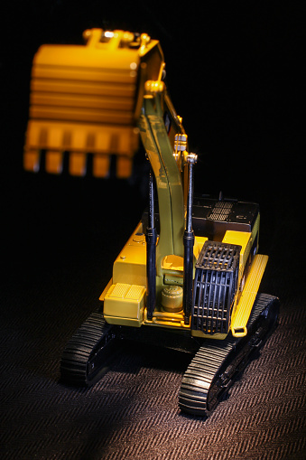Scale model backhoe on top of a textured black fabric as blurry foreground.