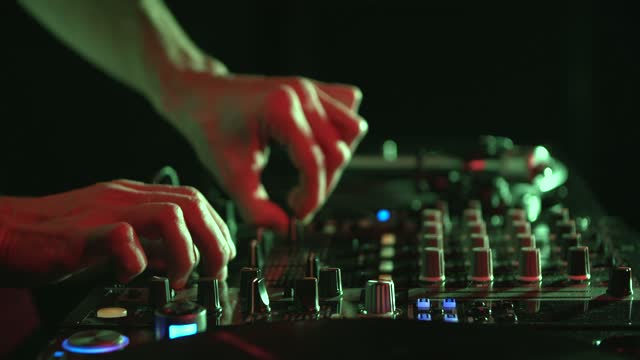 Hands of a DJ mixing music with sound mixer device in close-up video clip. Professional disc jockey plays set on stage