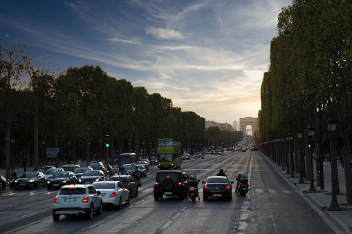 As the sun is setting on Paris, a glimpse at the traffic on the Avenue des Champs-Elysées with the Arc de Triomphe visible in background.