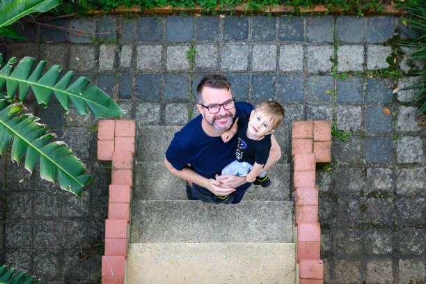 Top view of a father carrying his baby son on his lap as he comes home up the stairs on a summer morning