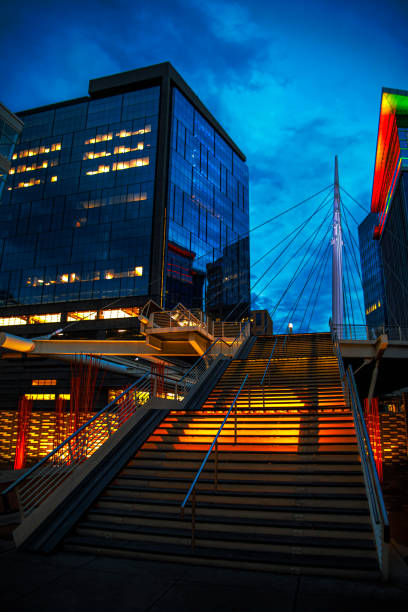 Night photo of the Millennium Bridge nestled between two buildings in lower downtown Denver. With colorful lights and a backlit staircase.