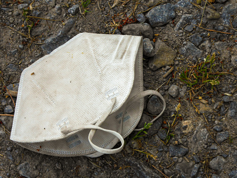 old, dirty and discarded FFP2-mask lies on agricultural road. A symbol of garbage and pollution.