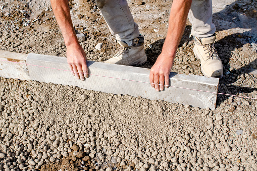 Builder placing edging pin kerb on semi-dry concrete using a string line to keep them straight during construction of the footpath