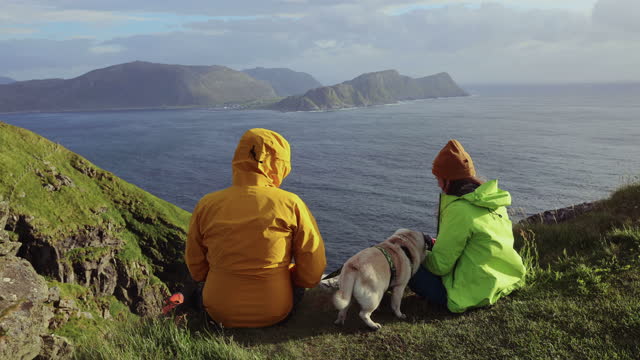 Rear view of woman and man relaxing with a dog conteplating sea view on Runde island, Norway