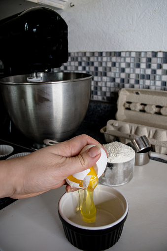 a mixed race woman is cracking an egg with one hand into a ramekin on a plastic cutting board while preparing some yummy cupcakes