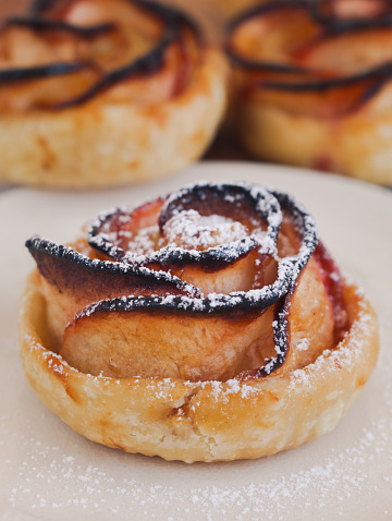 Close up of mini baked caramelized apple rose tarts rolled in a rose form with puff pastry. Sprinkle with icing sugar