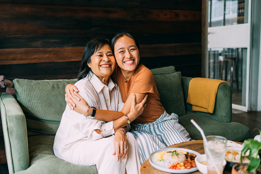The love between a mother and daughter is forever: a smiling Asian female embracing her mother. They are looking at camera.