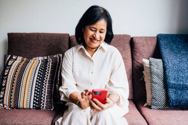 istock A Happy Beautiful Senior Woman Watching Something On Her Mobile Phone While Sitting On Her Cozy Sofa 1459436649