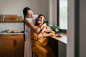 A Happy Beautiful Woman Hugging Her Mother While She Is Sitting In The Kitchen And Drinking Tea