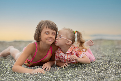 Portrait of a beautiful girl with a lovely little sister with Down syndrome on the beach