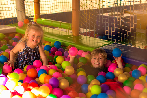 Portrait of two funny little kids playing in ball pit and enjoying time in childrens entertainment and play area, copy space
